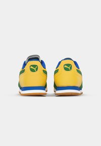 Αθλητικά παπούτσια Puma με κίτρινο δέρμα, μπλε διχτυωτές λεπτομέρειες, πράσινες ρίγες και λευκή σόλα. Διαθέτουν ασημί τακούνι και λεπτομέρεια λογότυπου.