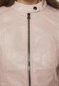 Giacca in pelle rosa chiaro con collo alto, cerniera frontale argento e chiusura con bottoni a pressione. Presenta dettagli cuciti sulle spalle.