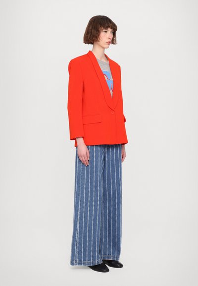 Red oversized blazer with a notched lapel, paired with wide-leg denim trousers featuring white vertical stitching and a grey graphic t-shirt.