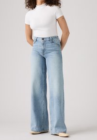 Ljusblå vida jeans med hög midja, tillverkade av denim, med en klassisk knapp- och dragkedjestängning samt framfickor.