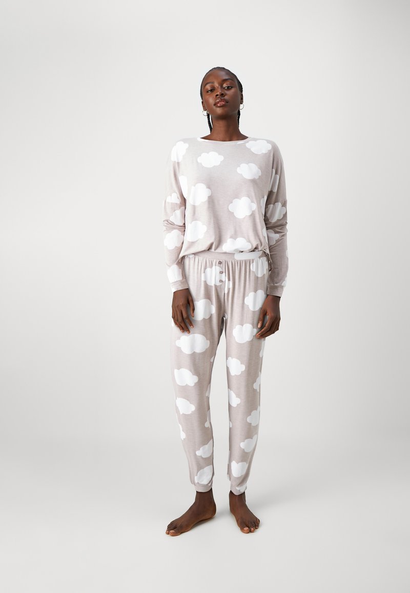 Ljusbeige loungewear-set med långärmad topp och matchande byxor, båda med vita molnmönster. Mjuk tyg, avslappnad passform.