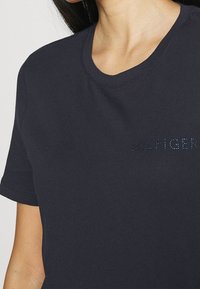 Námorně modré bavlněné tričko s kulatým výstřihem, krátkými rukávy a značkovým logem z modrých kamínků vpředu.