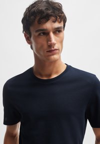 Marineblå kortærmet t-shirt lavet af struktureret stof, med rund halsudskæring og et diskret mønster på overfladen.