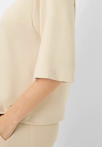Beige kortærmet top med en glat tekstur, afslappet pasform og en subtil sømdetalje nær bunden og ærmerne.