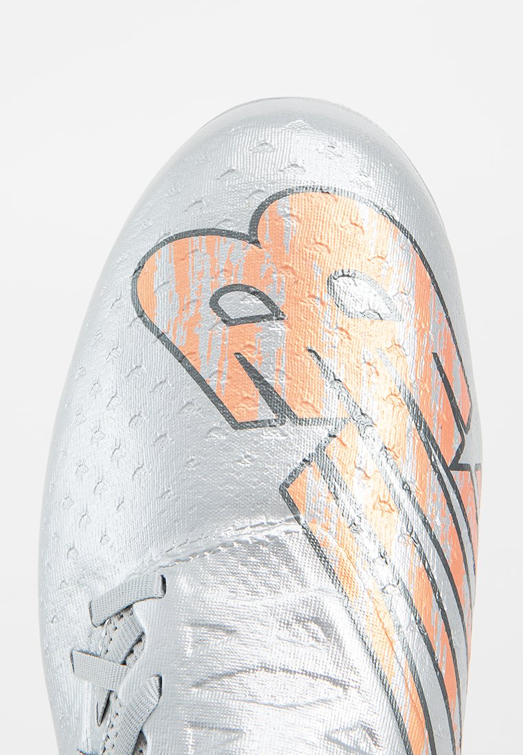 Crampon de football argenté avec un dessus texturé, présente un design graphique orange et noir. Comprend des lacets et une forme épurée pour la performance.