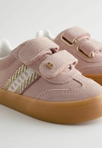 Roze antilopne tenisice s dva čičak traka, bijelim obloženjem, zlatnim detaljima i smeškim gumiranim potplatima. Imaju pleteni dizajn sa strane.