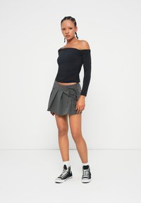 Crni top s otkrivenim ramenima s nabranim detaljima, sivi plisirani suknja s bočnim vezanjem i crne visoke tenisice s bijelim potplatima.