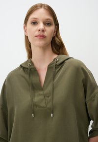 Felpa verde oliva con scollo a V, coulisse con estremità metalliche e vestibilità rilassata. Realizzata in un tessuto texturizzato con finitura opaca.