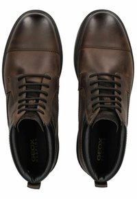 Botas de tobillo de cuero marrón con puntera redonda, diseño con cordones y acabado texturizado. Presenta un forro negro liso y un logotipo en el interior.