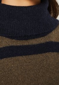 Pruhovaný rolák v hnědé a námořnické modři, vyrobený z jemného, texturovaného úpletu s vysokým límcem a kontrastními barevnými pásky.