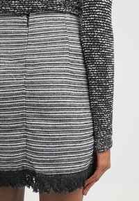 Vestido de rayas en blanco y negro con líneas horizontales, tejido texturizado y un dobladillo de encaje negro con flecos. Las mangas largas presentan un patrón similar.