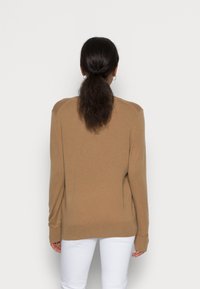 Ruskea neulepusero, jossa rento istuvuus, pitkät hihat ja resorireunukset, kuvattu takaa yksinkertaisella taustalla.