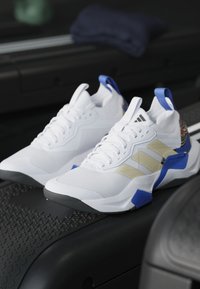 Scarpe da ginnastica bianche con strisce beige e accenti blu posizionate su una superficie nera texturizzata del tapis roulant.