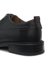 Schwarzer Leder-Herrenschuh mit dicker Sohle, "HUGO"-Markenetikett an der Seite und rot gefüttertem Zuglasche an der Ferse.