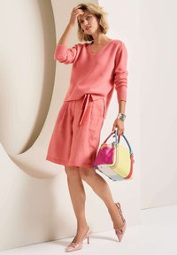 Rosa Kaschmir-V-Ausschnitt-Pullover, passende Leinen-Shorts, rosa Slingback-Pumps und eine mehrfarbige Handtasche mit verschiedenen Texturen und Griffen.
