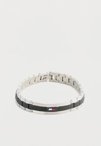 Pulsera de metal con secciones alternas en plata y negro texturizado, que presenta un pequeño acento de logo en rojo, blanco y azul.