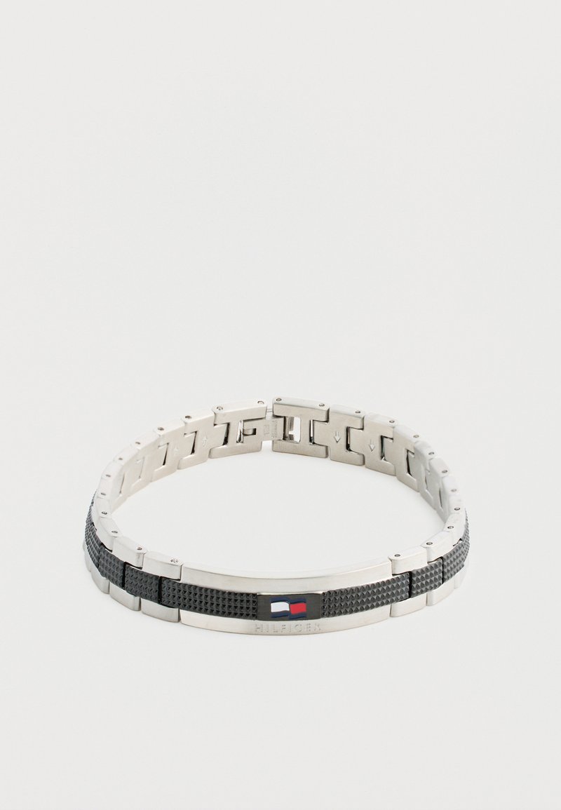 Pulsera de metal con secciones alternas en plata y negro texturizado, que presenta un pequeño acento de logo en rojo, blanco y azul.