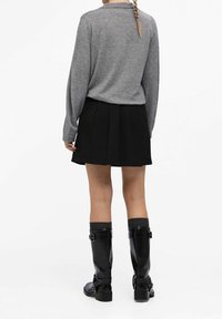 Szary sweter z długimi rękawami w połączeniu z czarną plisowaną spódnicą. Modelka nosi czarne kozaki do kolan z klamrami i prążkowane szare skarpetki.