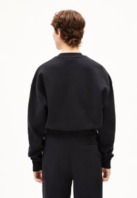 Zwarte sweatshirt met een relaxte fit, featuring verlaagde schouders en een ronde hals. Gladde textuur en elastische zoom, gecombineerd met bijpassende broeken.