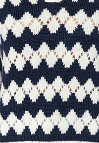 Primo piano di un tessuto lavorato a maglia blu navy e bianco con motivi a zigzag e a diamante alternati in righe orizzontali.