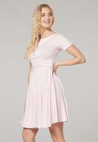 Kurzärmeliges, hellrosa Kleid mit einem taillierten Oberteil und einem ausgestellten Rock. Weicher Stoff, glatte Textur und knielanger Saum.