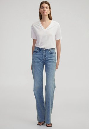 White V-neck t-shirt paired with high-waisted light blue denim flared jeans. Smooth texture, visible stitching, and a classic fit. Black sandals.