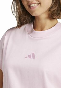 T-shirt di cotone rosa chiaro con maniche corte e colletto rotondo. Presenta un piccolo logo lucido sul petto in un design a gradiente di rosa scuro.