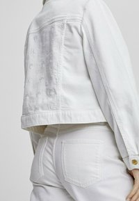 Vit denimjacka med broderade detaljer på baksidan, med en kort design, knappstängning och klassisk krage.