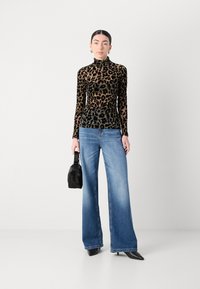 Een leopardprint coltrui van fluweel, gecombineerd met lichtblauwe wijde jeans. Het model houdt een kleine zwarte handtas vast en draagt zwarte puntige hakken.