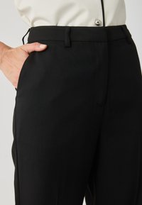 Fekete testre szabott nadrág sima textúrával, oldalsó zsebekkel és klasszikus szabással. A derékpánt övhurkokkal van ellátva az állítható méret érdekében.