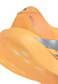 Orange athletic shoe featuring a textured upper, silver accents, and a cushioned sole with white cutouts for improved traction.