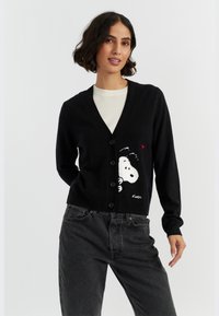 Cardigan nero realizzato in tessuto morbido, caratterizzato da una grafica di Snoopy bianca e un cuore rosso. Ha un collo a V, una chiusura con bottoni e una vestibilità slim.