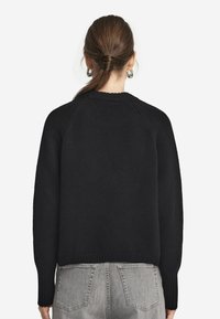 Svart stickad tröja med rund halsringning, raglanärmar och ribbade ärmslut. Tyget har ett strukturerat mönster och är matchat med grå höga jeans.