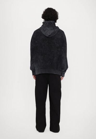 Haut de sweat à capuche noir surdimensionné avec une finition texturée, doté d'une capuche à cordon de serrage et de poignets côtelés, associé à un pantalon noir ample.