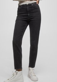 Jean noir taille haute avec une coupe slim, design à cinq poches et légère décoloration, associé à des baskets blanches montantes.