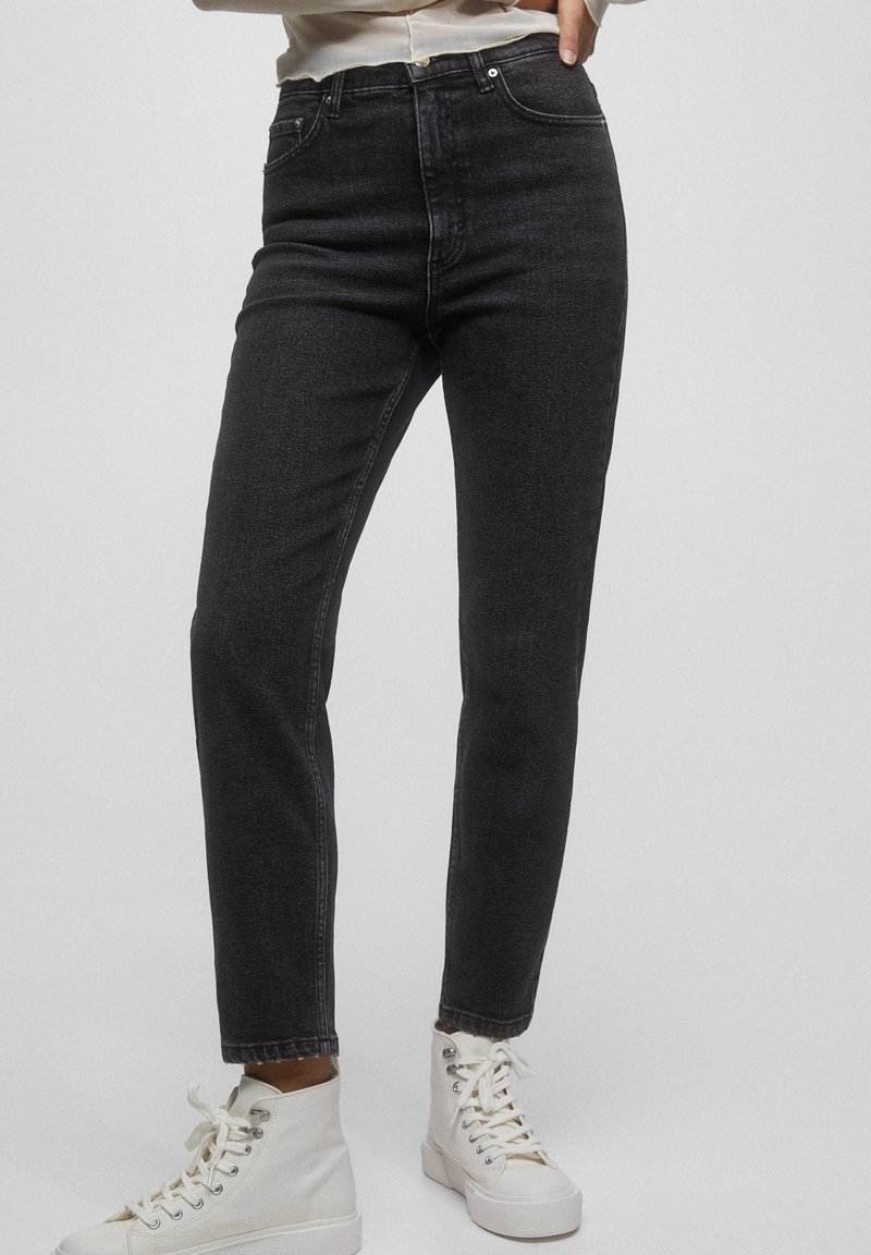 Jean noir taille haute avec une coupe slim, design à cinq poches et légère décoloration, associé à des baskets blanches montantes.