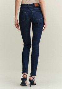 Jeans ajustados de mezclilla de color azul oscuro, con un parche de cuero marrón en la parte trasera de la cintura y dos bolsillos traseros.