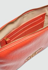 Koralfarvet læderclutch med struktureret overflade, guld lynlås og indvendige lommer, herunder en lynlåssektion og brandlogo.