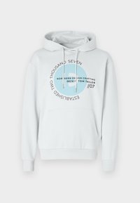 Sudadera de color gris claro hecha de mezcla de algodón. Presenta un bolsillo canguro, capucha ajustable con cordones y un estampado gráfico circular en azul y negro.