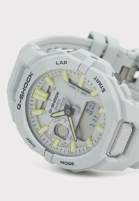 Montre G-SHOCK en gris clair avec des accents jaunes. Présente un affichage analogique-numérique, des boutons texturés et un design de boîtier robuste et multifacette.