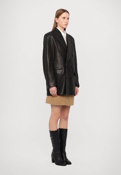 Melna ādas dubultās krūšu blazera, asie apkakles, sānu kabatas, apvienota ar brūnu vilnas svārku un melniem augstiem zābakiem ar papēdi.