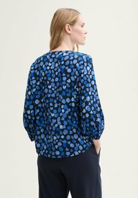 Blusa a maniche lunghe blu e nera con motivo a pois. Caratterizzata da un collo rotondo e maniche leggermente gonfie. Tessuto morbido.