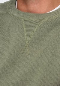 Felpa verde oliva con scollatura a girocollo a costine e motivo a maglia tessuta. Presenta un dettaglio a punto croce sul collo. Materiale in cotone morbido.