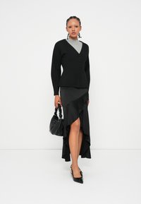 Černý kardigan s knoflíky, šedé tričko, asymetrická černá sukně s volánky, černá kabelka s texturovanou rukojetí, černé špičaté boty.