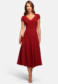 Red, knee-length dress with a fitted bodice, cap sleeves, and a flared skirt. Smooth fabric with a v-neckline. Paired with a clutch and heels.