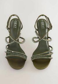 Sandali con tacco alto verde a strisce con pietre decorative in argento sui laccetti e una forma della punta liscia e arrotondata.