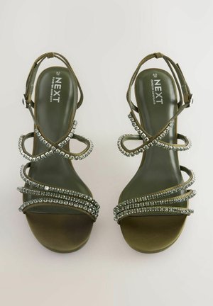 Green strappy high-heeled sandals with decorative silver rhinestones on the straps and a smooth, rounded toe design.