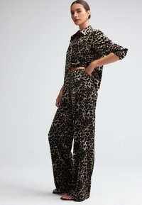 Leopardprint to-delt sæt, der har en løstsiddende, skjortekravebluse og brede benbukser i et blødt, tekstureret stof.