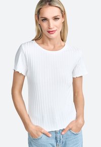 T-shirt blanc à col rond avec des manches courtes et volantées. Le tissu semble doux et léger, associé à un jean en denim.