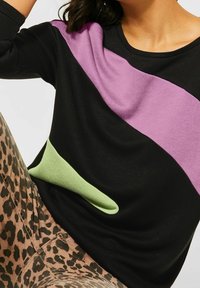 Svart tröja med diagonala lila och gröna färgblock. Har en mjuk textur och en stor grön accentficka. Bärs med byxor i leopardmönster.